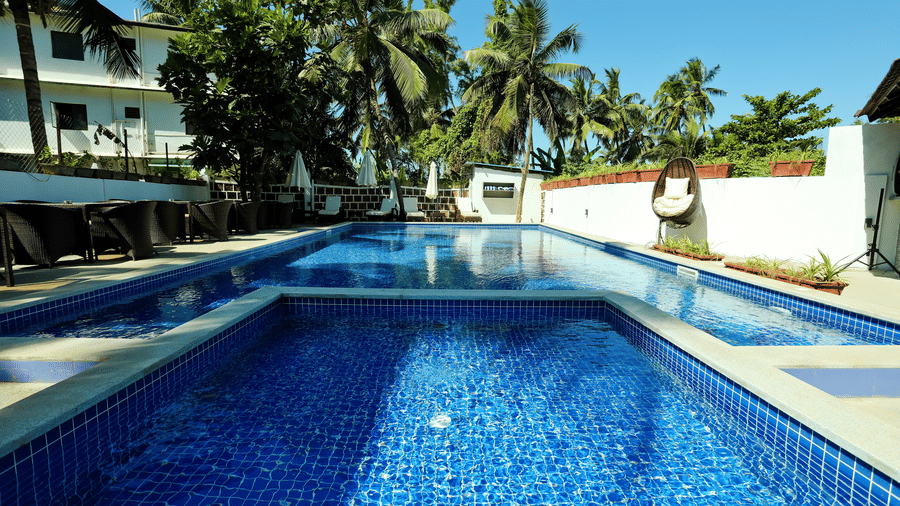A swimming pool with trees on one side of it at Amara Grand Baga, Goa.